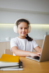 Young girl engages in online learning with headphones in a cozy study environment during the daytime