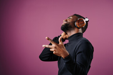 Young Black man enjoying music with headphones, wearing a stylish black turtleneck, expressing joy...