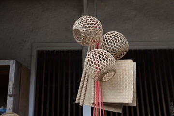 A cluster of woven bamboo crafts—spherical baskets and mats—hang with red strings against a wooden slatted backdrop.
