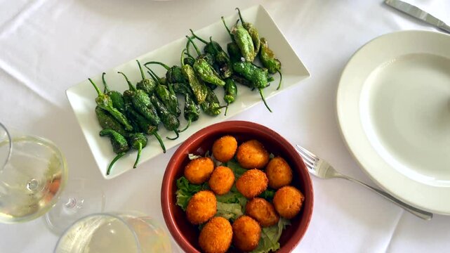 Eating tapas,  ham and fish croquettes, green grilled peppers, pimientos de padron on holiday in Spain