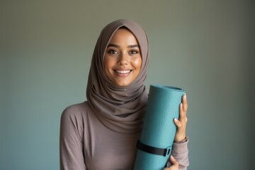 Portrait of happy biracial woman wearing hijab, holding yoga mat and smiling