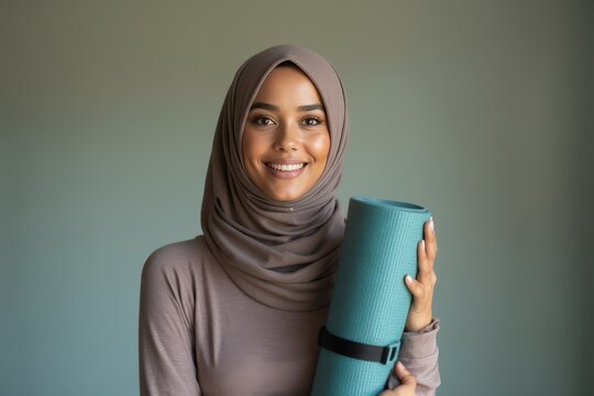 Portrait of happy biracial woman wearing hijab, holding yoga mat and smiling
