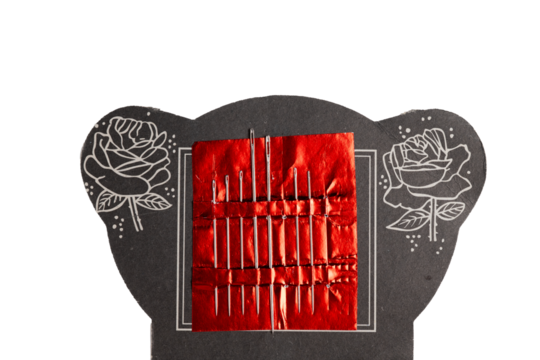 Set of metal sewing needles on red foil with decorative card
