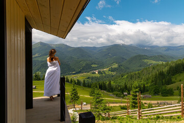 Woman wrapped in white blanket overlooking green mountain valley. A barefoot woman wrapped in a...