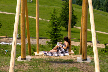 Woman reading book on wooden swing outdoors. A woman wrapped in a blanket relaxes on a large wooden...