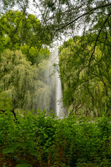 Obraz premium Majestic fountain surrounded by lush greenery in a serene park during a cloudy afternoon
