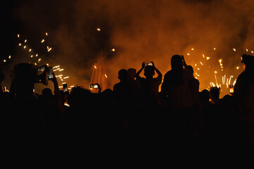 Silhouetted crowd holds smartphones to record light show with fireworks. People capturing an event...