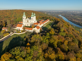 Active Camaldolese monastery and baroque church in a wood on the hill in Bielany, Krakow, Poland. Aerial view in sunset light in fall with Vistula River and far view of Cracow city in the background