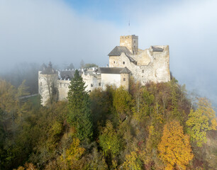 Poland. Medieval castle in Niedzica, dating to 14th century (upper castle) in autumn in October in morning fog. Trees in beautiful fall colors. Sunrise light. Aerial drone view
