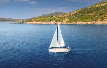Obraz premium Aerial view of beautiful sailboat. Boat on the sea at sunset in summer. Lefkada island, Greece. Top view of luxury yacht, sail boat, clear blue water, sky, mountain. Travel. Cruise vacation. Yachting