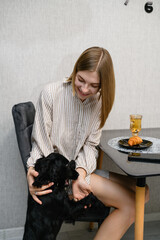 Smiling woman cuddling black cocker spaniel puppy at breakfast table.
