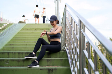 Woman Checking Smartwatch While Resting on Green Stairs in Urban Park During Evening Workout