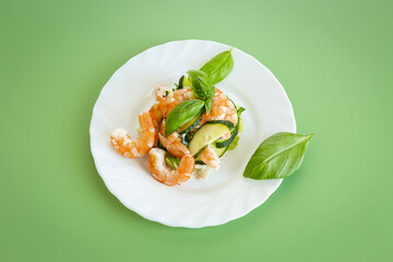 Fresh vegetable salad with shrimps and cucumbers on a green background