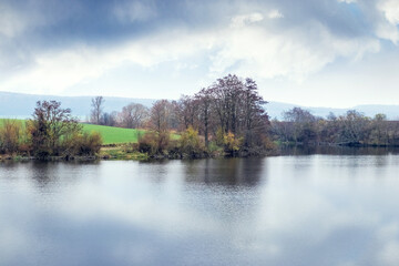 Autumn river landscape calm water cloudy sky reflection colorful trees banks green field horizon...