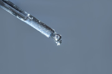 Close-up of transparent dropper with droplet on light blue background.