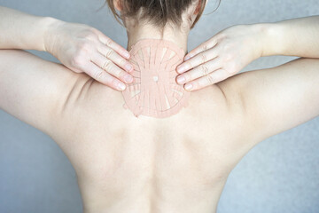 Female adult applying therapeutic patch on upper back for pain relief and healing.