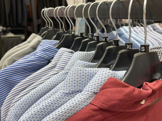 A neat row of various men's shirts, including striped, patterned, and solid colors, hangs on black...