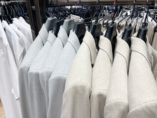A close-up shot of a rack of light-colored, casual men's blazers and shirts, showcasing their...
