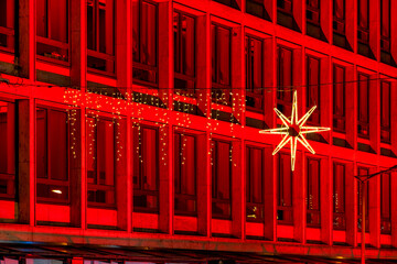 A bright Christmas star and twinkling fairy lights adorn a red illuminated modern building in Marburg's city center