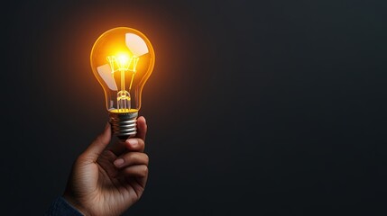 Hand holding glowing electric lightbulb illuminated with warm yellow light against dark background