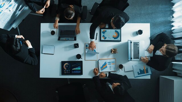 Top down aerial view of smart boss invites project manager to explain about marketing plan at white board. Group of diverse investor listen presentation while working and analyze chart. Directorate.