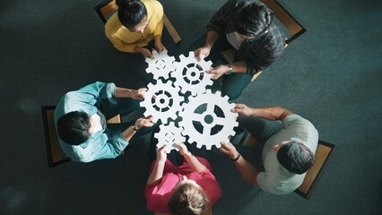 Top view of smart business people joining and gathering white gear together. Aerial view of diverse...