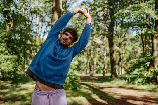 Young man stretching arms in wooded park during workout