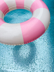 Swimming ring with pink and white stripes in a blue outdoor pool. Poolside atmosphere. Pink float.