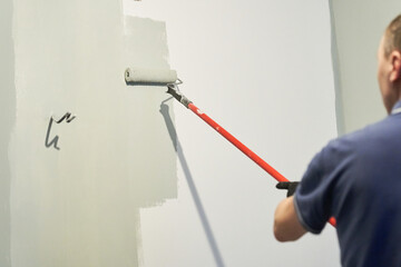 Men's hands paint walls with a roller, work painting on the surface, painting walls in an apartment, repair with white paint. With space to copy. High quality photo
