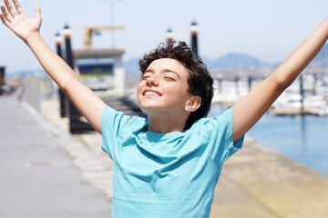 portrait of teenage boy with open arms inhaling sea breeze in the sun
