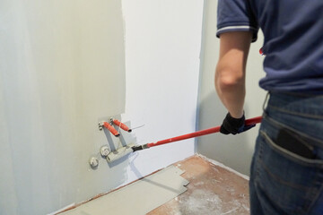A man paints the inner wall of his house. Apartment renovation. Concrete walls are painted with a paint roller. High quality photo