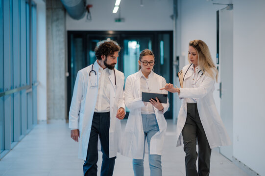 Doctors walking and discussing patient chart on digital tablet in hospital corridor