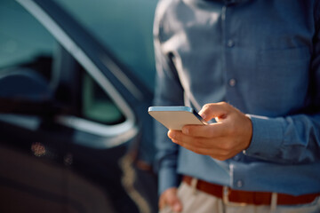 Close up of man using app on cell phone next to his car.