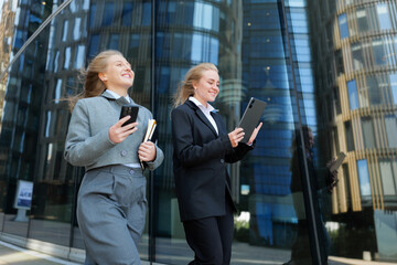 Business professionals in smart attire engage with devices while walking in a modern urban setting...