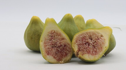 close-up of a group of green figs, one of which is cut in half, on a white background