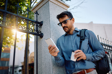 Below view of entrepreneur with takeaway coffee using cell phone on street.