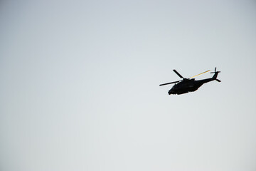 Silhouette of a helicopter flying at sunset with warm orange and red tones in the sky. Dramatic aviation scene on a colorful twilight background.

