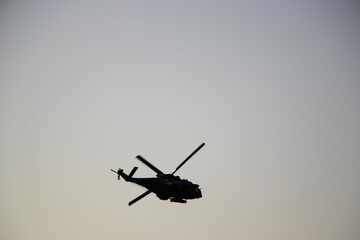 Silhouette of a helicopter flying at sunset with warm orange and red tones in the sky. Dramatic...