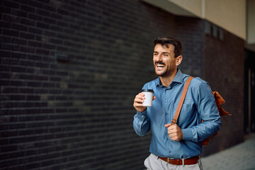 Happy businessman drinking takeaway coffee while walking outdoors.
