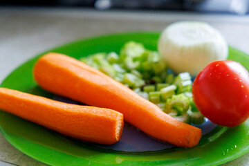 
Fresh vegetables are displayed on a green plate, including two peeled carrots, sliced ​​celery stalks, half an onion, and one tomato.