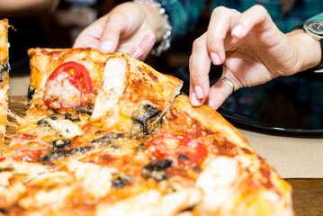 Women's hands break off a piece of pizza
