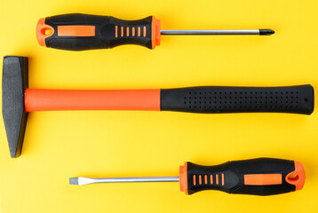 Pair of screwdrivers and hammer on bright yellow background, top view tools