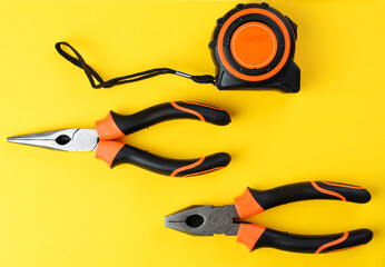 Pair of pliers and tape measure on bright yellow background, top view