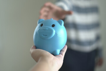 One hand is holding the piggy bank and another hand putting cash note for financial saving for the...