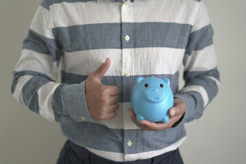 Young asian man is holding the piggy bank and putting cash coins for financial saving for the...