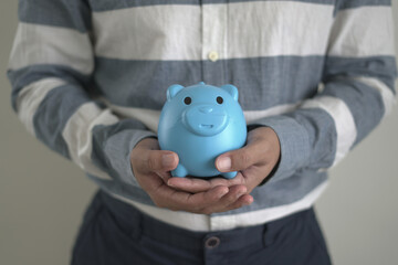 Young asian man is holding the piggy bank and putting cash coins for financial saving for the...