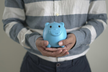 Young asian man is holding the piggy bank and putting cash coins for financial saving for the...