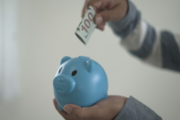Young asian man is holding the piggy bank and putting cash coins for financial saving for the...