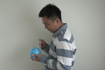 Young asian man is holding the piggy bank and putting cash coins for financial saving for the...
