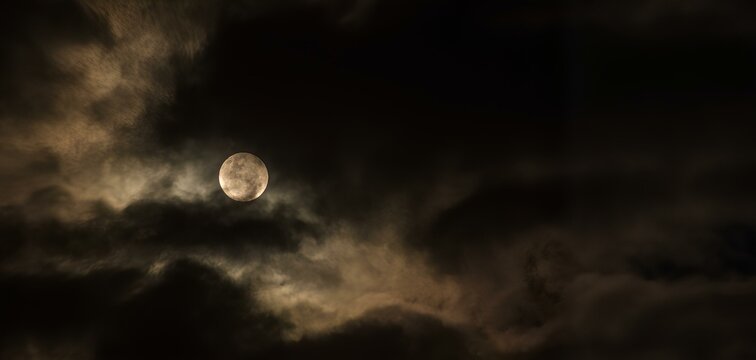 Bright full moon shines through floating, dark, dramatic clouds.  For Halloween-themed design, mysticism or magic, weather forecast, background for text